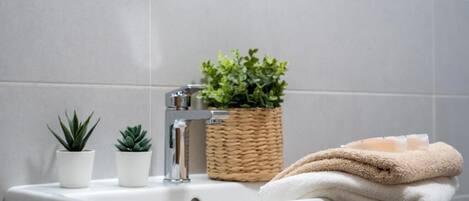 Un lavamanos de baño con dos plantas en macetas, una cesta tejida y una pila de toallas.
