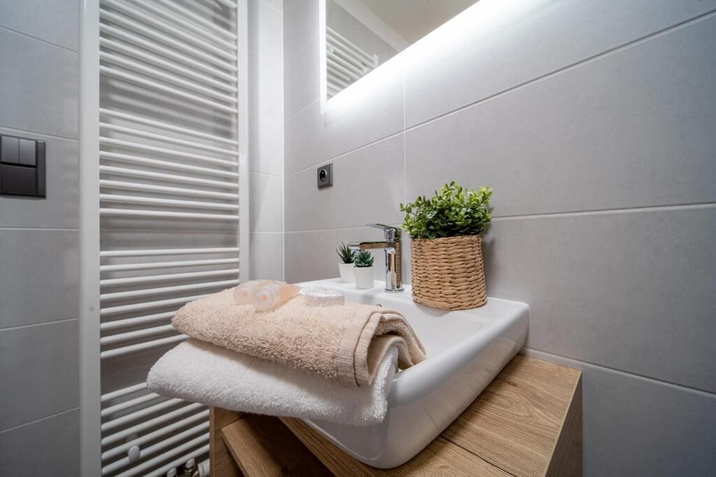 A modern bathroom with a white sink, a small potted plant, and a towel on the counter.