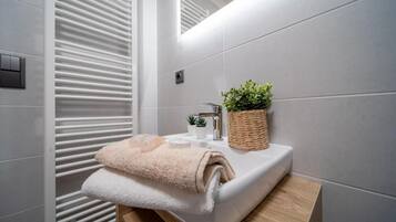 Un baño moderno con un lavabo blanco, una pequeña planta en maceta y una toalla en la encimera.