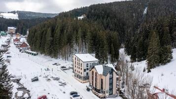 Lumipeitteinen kaupunki, jonka siluettia hallitsee modernilla arkkitehtuurilla varustettu huomattava rakennus. Kaupungin ympärillä on tiheä metsä, ja taustalla näkyy laskettelurinne.