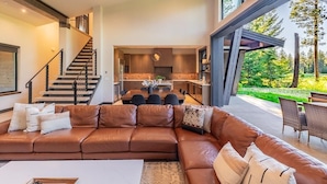A modern interior with a brown leather sofa, a dining area, and a kitchen. - Golf Course View, Fire Pit & Suncadia Pool Access (Cle Elum)