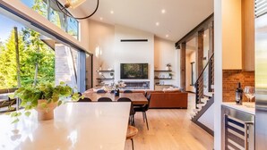 A modern kitchen with a large island, a dining area with a sofa, and a TV mounted on the wall. - Golf Course View, Fire Pit & Suncadia Pool Access (Cle Elum)
