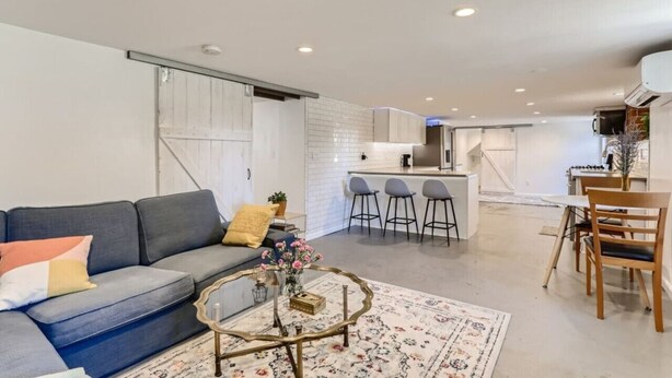 A modern living room with a sofa, coffee table, and a kitchen area with bar stools. - Pet Friendly I Remodeled I Near RiNo | Sleeps 7 (Denver)
