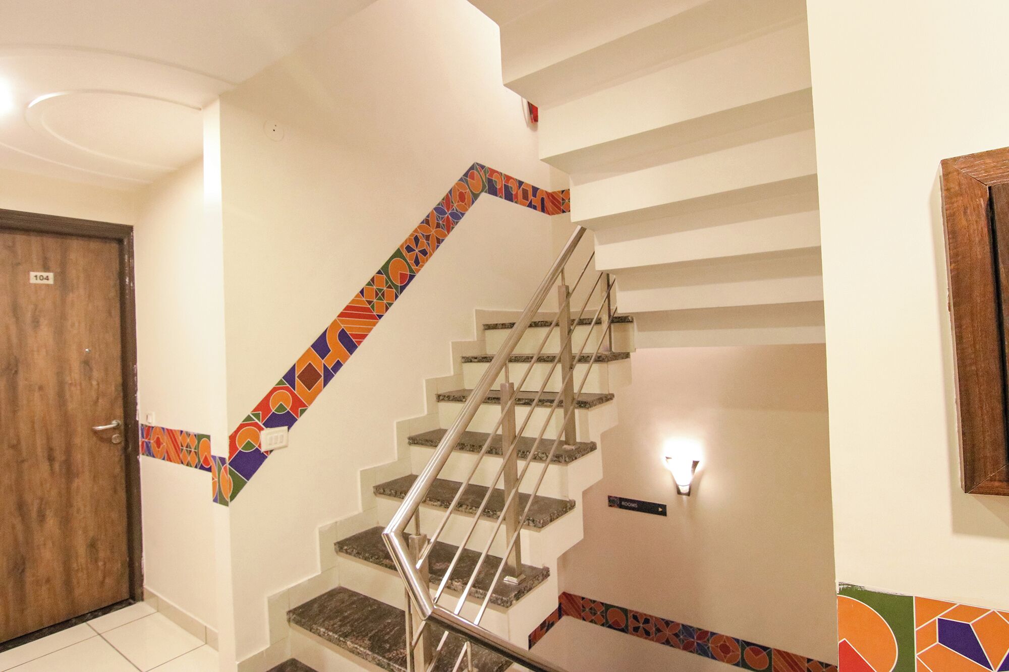 A staircase with a handrail, white walls, and a colorful border.