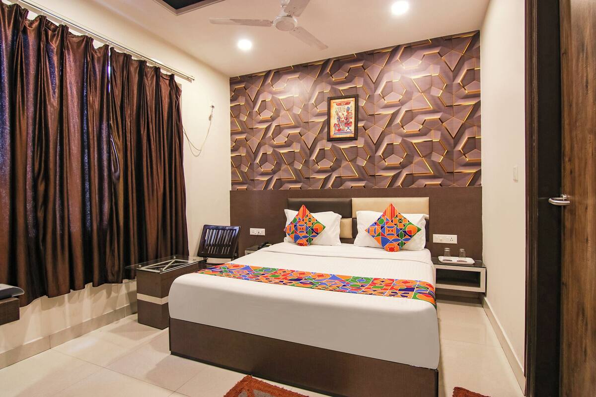 Quarto moderno com cama grande, painel decorativo na parede, ventoinha no teto e mesa de cabeceira.