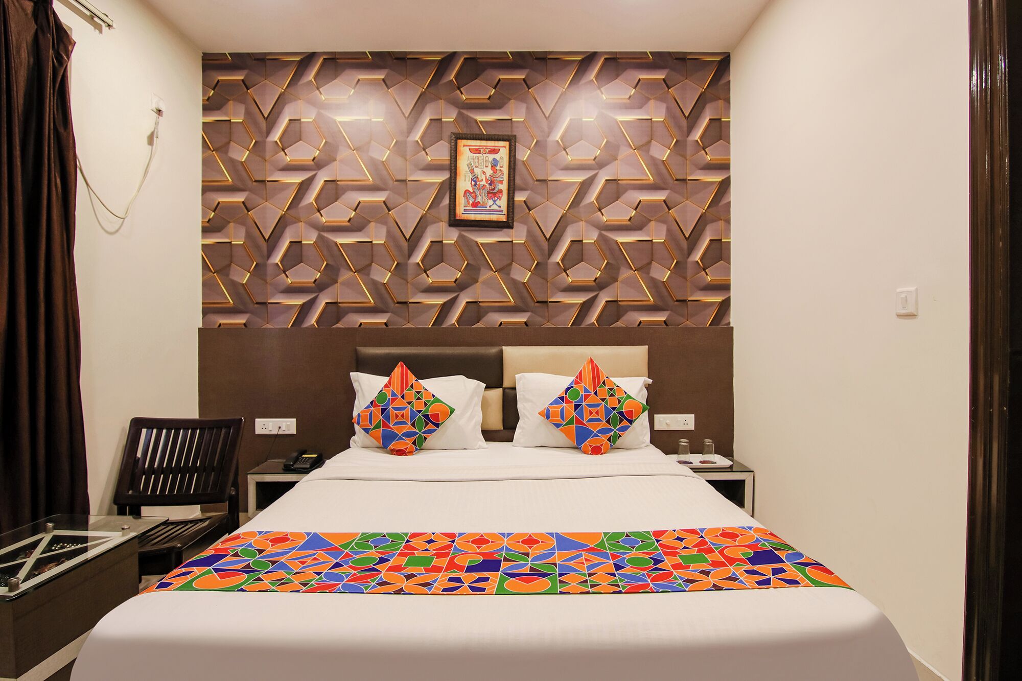 Habitación de hotel con cama, mesita de noche, teléfono y pared con diseño geométrico.
