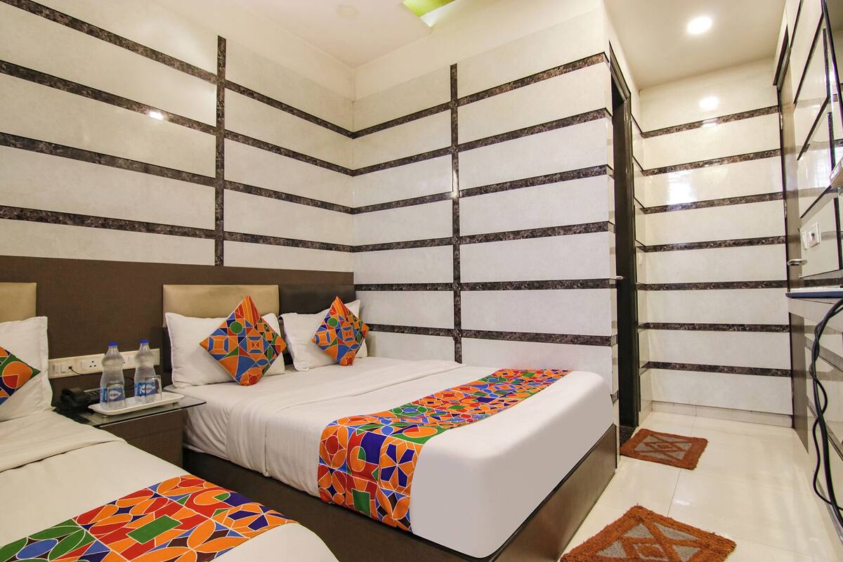 Quarto de hotel com uma cama grande, mesa de cabeceira com telefone e garrafas de água, e manta colorida.