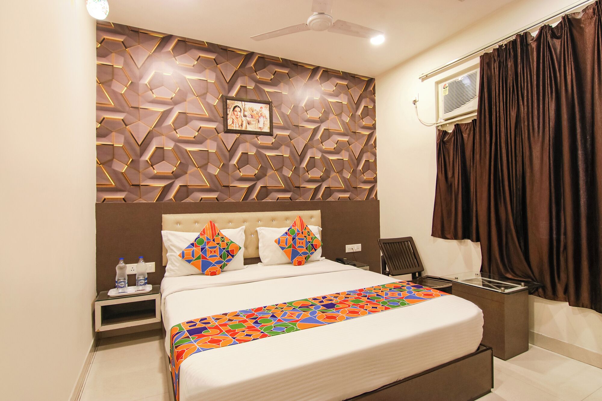 A hotel room with a bed, a nightstand, a desk, a chair, a ceiling fan, and a window with curtains.