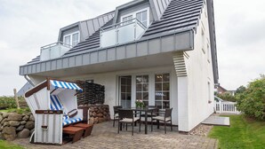 A house with a patio area featuring a table and chairs, a wicker chair, and a stone wall. - Strandnahe 3-zimmer Ferienwohnung auf ca. 55m² Wohnfläche, für bis zu 4 Personen (Wenningstedt-Braderup (Sylt))