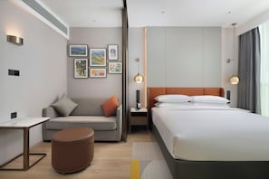 Habitació d'hotel moderna amb un llit, un sofà, una taula petita i una taula de nit amb una làmpada.