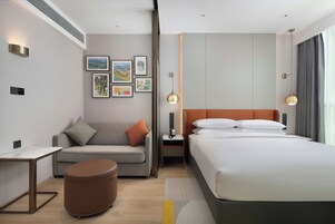 Una habitación de hotel moderna con una cama, un sofá, una mesita y una lámpara en la mesita de noche.
