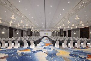 Un salón de conferencias con hileras de sillas, piso alfombrado y candelabros.