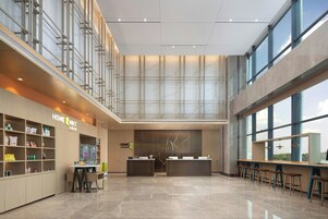 Un amplio vestíbulo con mostrador de recepción, barra de café y zona de estar, techos altos y ventanas grandes.