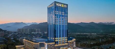 Ein modernes Hotel mit einem gut sichtbaren 'HOME 2 SUITES'-Schild, umgeben von einer Stadtlandschaft und Bergen.