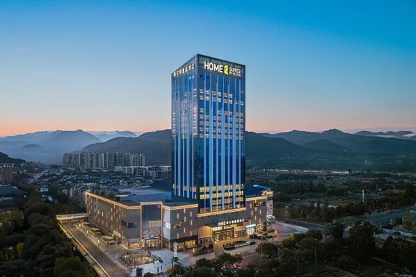 A modern hotel with a prominent 'HOME 2 SUITES' sign, surrounded by a cityscape and mountains.