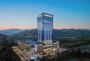 Un moderno edificio de hotel con un diseño vertical llamativo, ubicado en un paisaje urbano con montañas al fondo.
