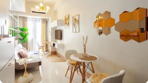 A modern living room with a sofa, a dining table, and a TV. There are hexagonal wall decorations and a plant. - MOA Staycation 10mins to Airport. 10mins walk to iconic Mall of Asia. (Pasay)