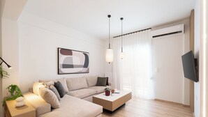 A modern living room with a sofa, a coffee table, pendant lights, and a flat-screen TV mounted on the wall.