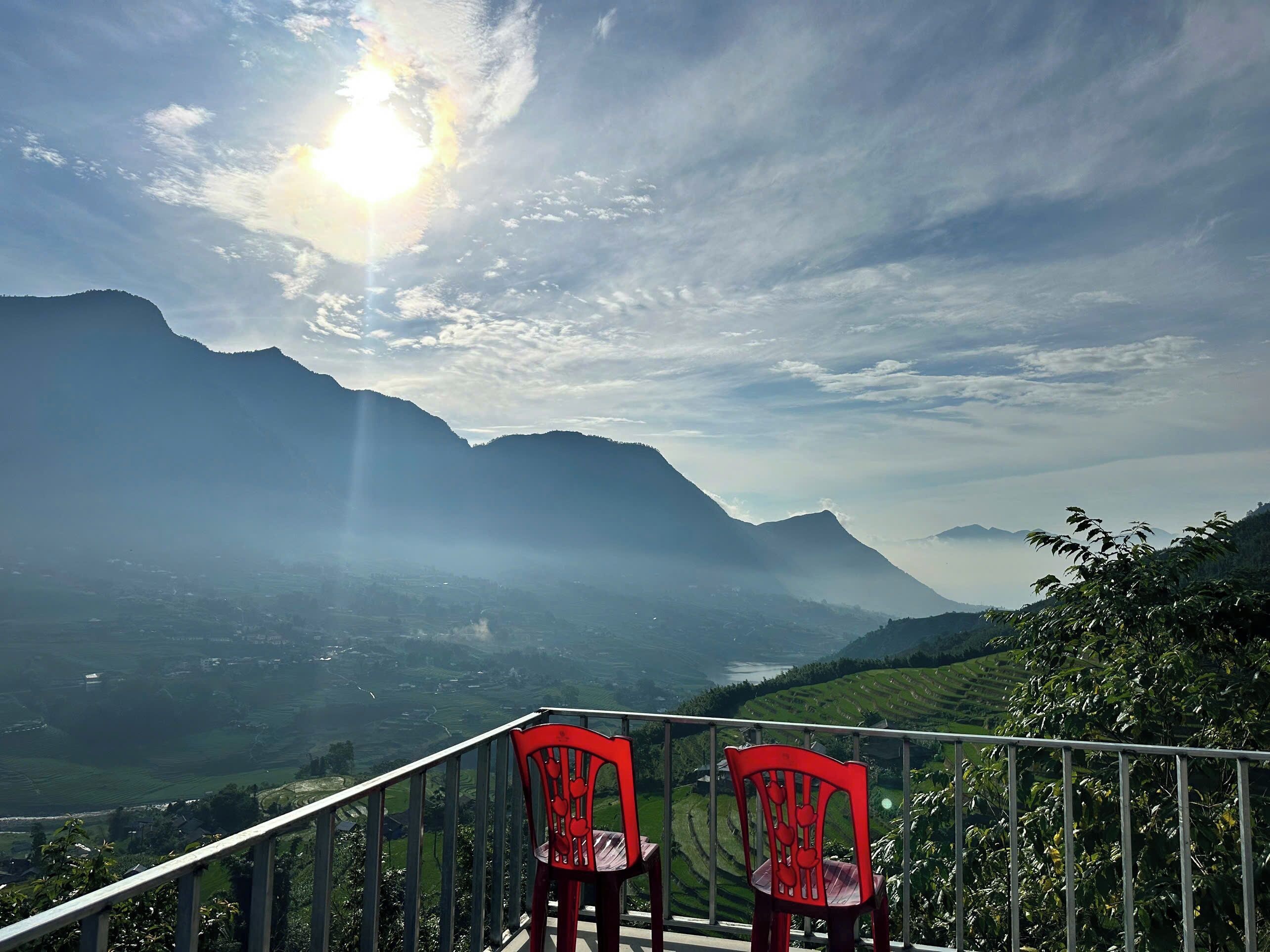 Un balcón con dos sillas rojas que ofrece vistas a un paisaje montañoso con un valle y un río.