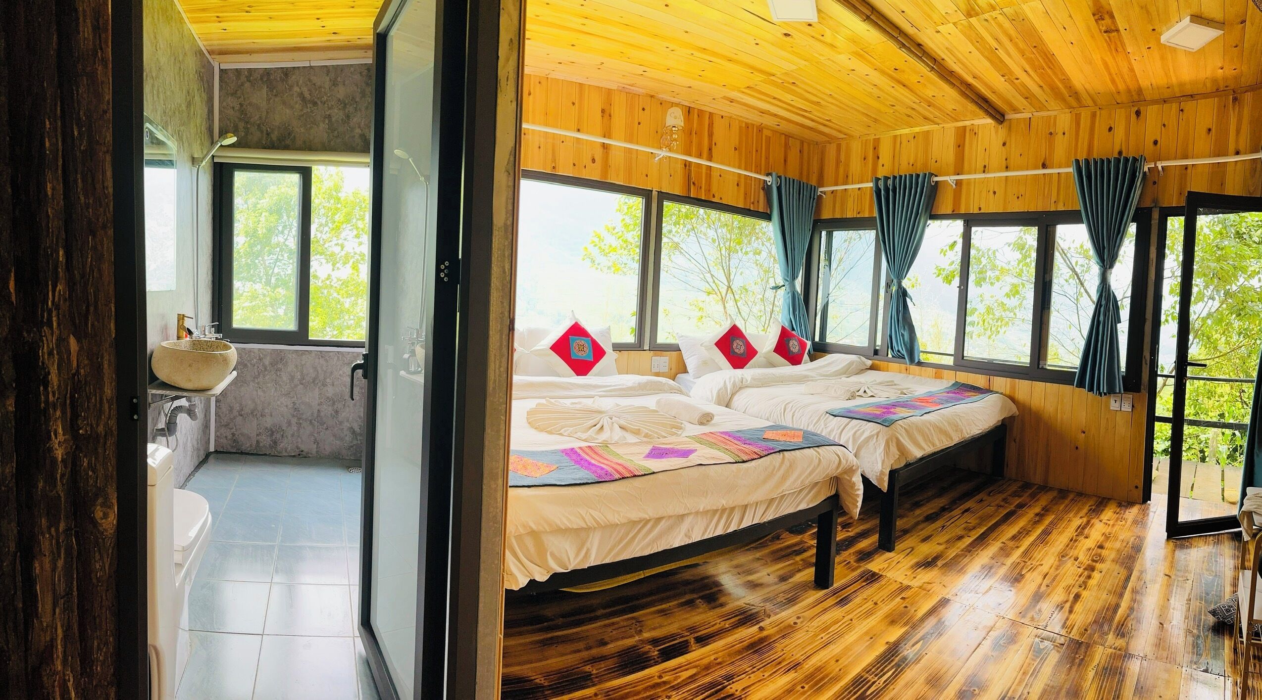 Ein Schlafzimmer in einer Holzhütte mit zwei Betten, einem Badezimmer mit Waschbecken und großen Fenstern.