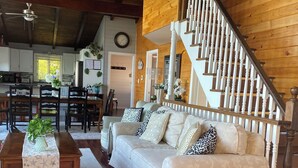 A spacious living room with a wooden staircase, a sofa set, and a dining area. - Huron Lakefront Cottage Charming 8 bedrms 4bths 18+guests 8car/Hotub/pets . (Goderich)