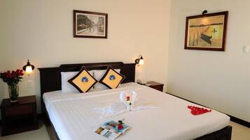 A neatly made bed with a swan and heart design, two pillows, a vase of red flowers, and a framed picture on the wall.