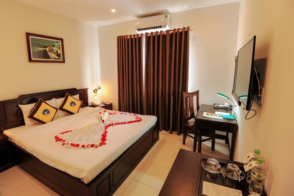 A hotel room with a bed, a desk, a television, and a window with curtains.