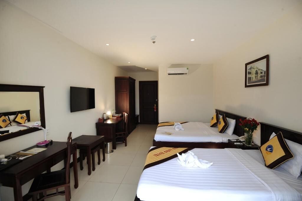 A hotel room with two beds, a desk, a chair, a flat-screen TV, and an air conditioning unit.