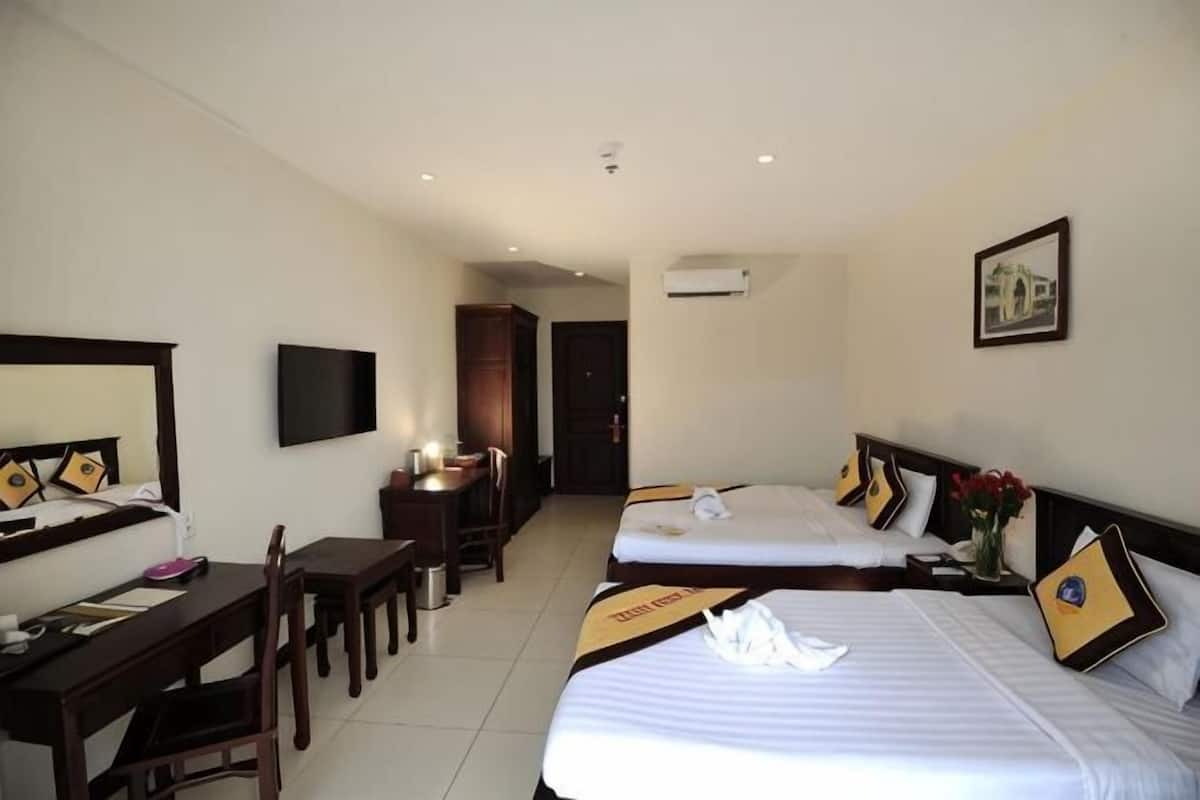 A hotel room with two beds, a desk, a chair, a TV, and a door leading to another room.