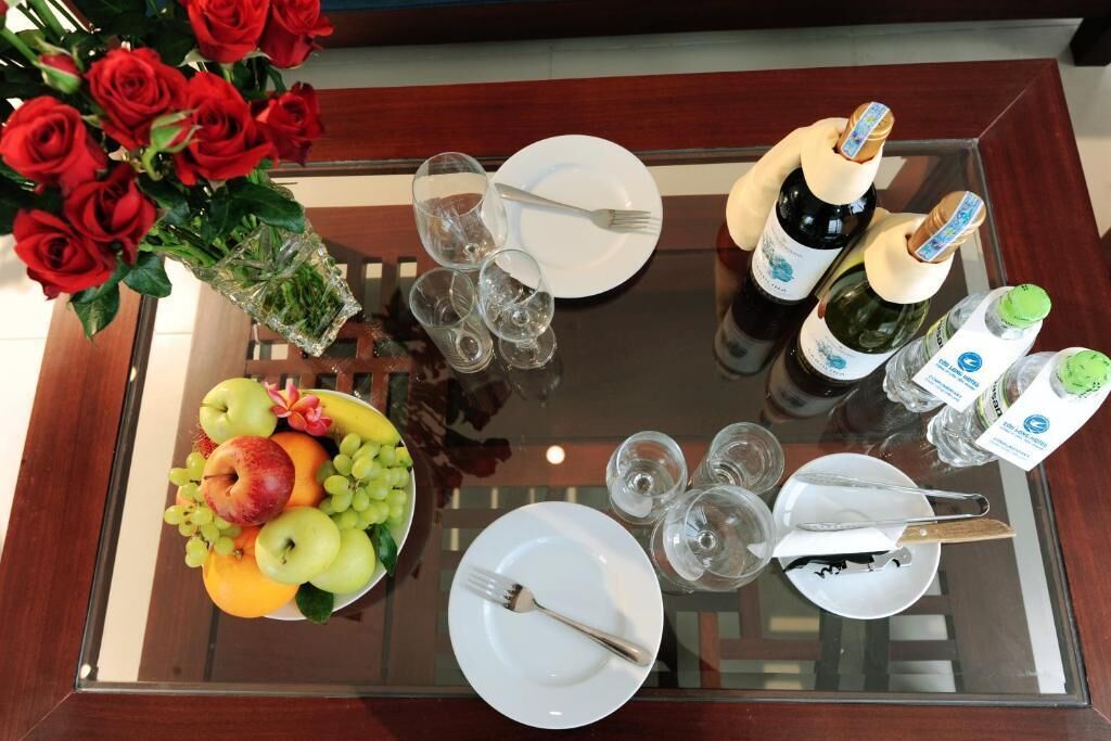Une table à manger avec un panier de fruits, des bouteilles de vin, des verres et des couverts.