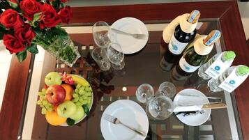 A dining table with a fruit bowl, wine bottles, glasses, and cutlery.