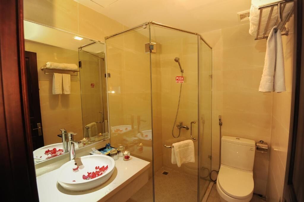 A modern bathroom with a glass-enclosed shower, a white sink with rose petals, and a toilet.