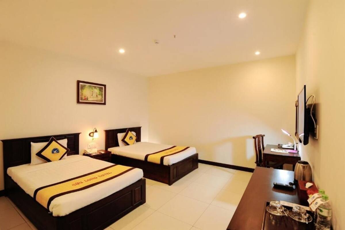 A hotel room with two beds, a desk, a chair, a TV, and a framed picture on the wall.