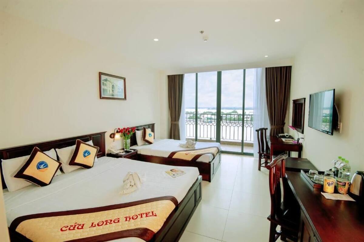 A hotel room with two beds, a TV, a desk with a chair, and a balcony with a view.