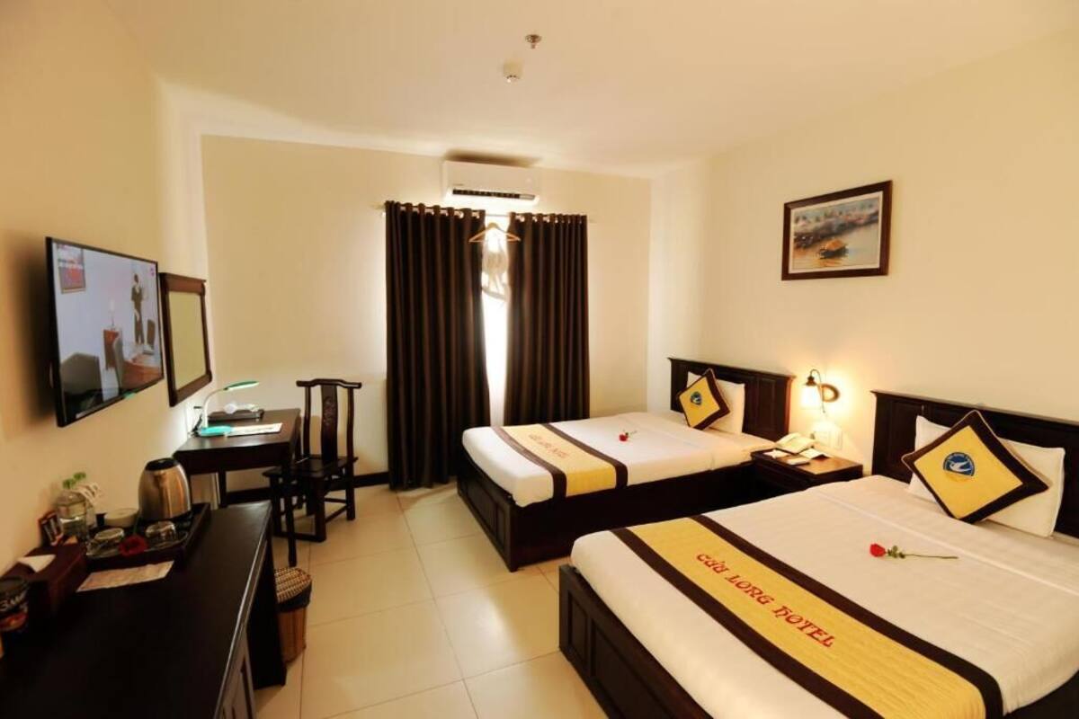 A hotel room with two beds, a desk, a chair, a TV, and a window with curtains.