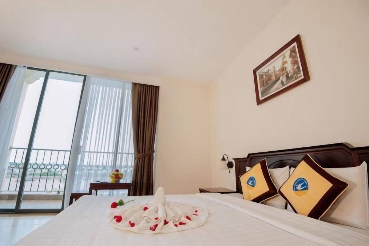 A hotel room with a bed, a framed picture on the wall, and a view of the outside through the window.