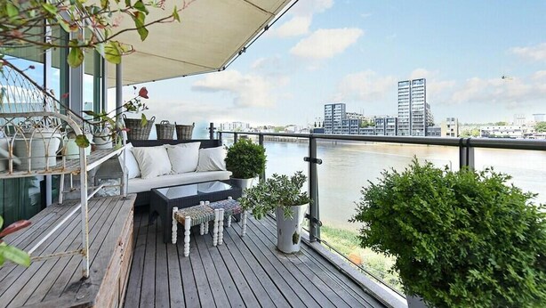 Una terraza con sofá y mesa, con vista a un río y edificios al fondo.
