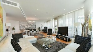 Una sala de estar moderna con un conjunto de sofás, una mesa de centro de vidrio, un televisor y un comedor con mesa y sillas.