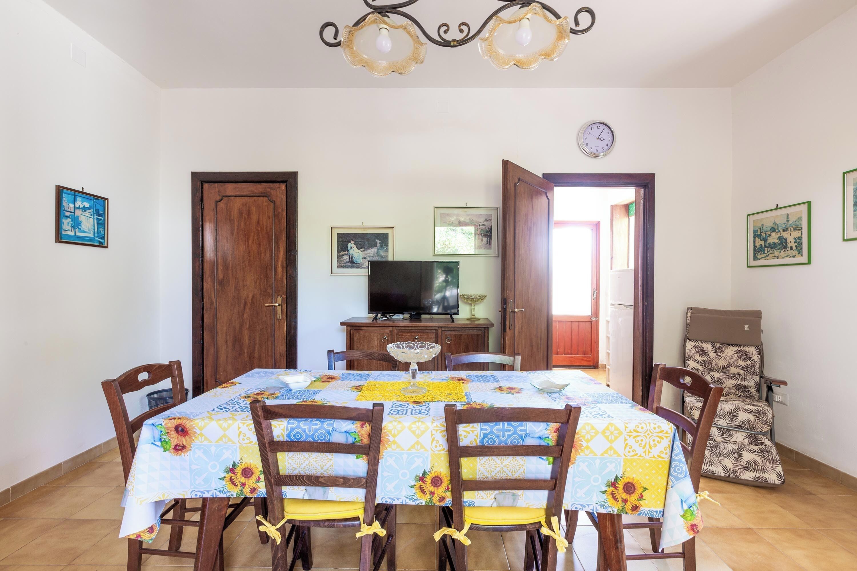 A dining area with a table set for four, surrounded by wooden chairs. A television is mounted on the wall above the table.