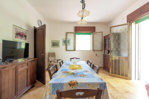 A dining area with a table set for four, wooden cabinets, a television, and a large window with blinds. - 4085 Villa Teresa Portoselvaggio by Barbarhouse (Nardò)