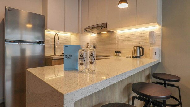A modern kitchen with a stainless steel refrigerator, a coffee maker, and two bar stools.