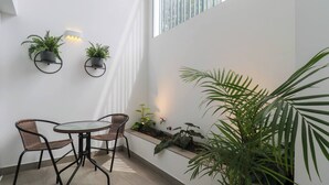A modern interior with a round glass table and two wicker chairs, surrounded by potted plants and a built-in planter.