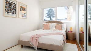 Un dormitorio con cama, almohadas, una mesita de noche con lámpara, y dos cuadros enmarcados en la pared.