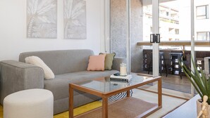Una sala de estar moderna con un sofá gris, una mesa de centro de madera y un ventanal que da a un área exterior con balcón.