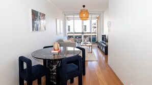 Una sala de estar moderna con una mesa redonda de mármol, sillas azul oscuro, un sofá gris y una lámpara colgante de ratán.