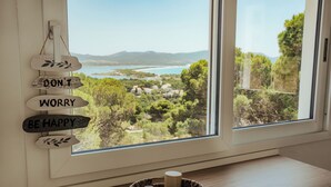 Vista a través de una ventana con un letrero de madera que dice 'DON'T WORRY BE HAPPY' y una bandeja de mimbre con dos tazas sobre una mesa de madera.