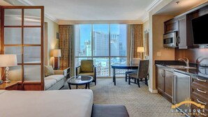 A hotel room with a large window, a bed, a sofa, a dining table, and a kitchenette. - Strip Views, King Bed & Jacuzzi | MGM Signature (Las Vegas)