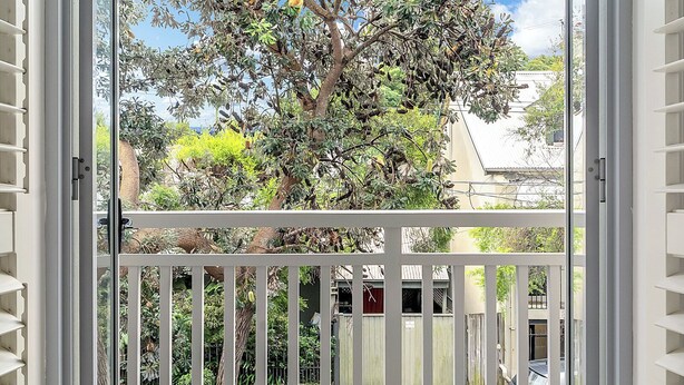 A view through an open door to a wooden deck with a white railing, a tree, and a clear blue sky. - The Newtowner - Stylish Home in the heart of Newtown! (Newtown)