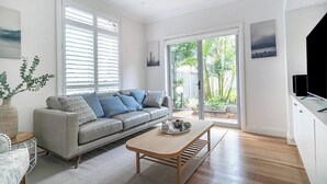 A modern living room with a grey sofa, wooden coffee table, and a view of a garden through large sliding glass doors. - The Newtowner - Stylish Home in the heart of Newtown! (Newtown)