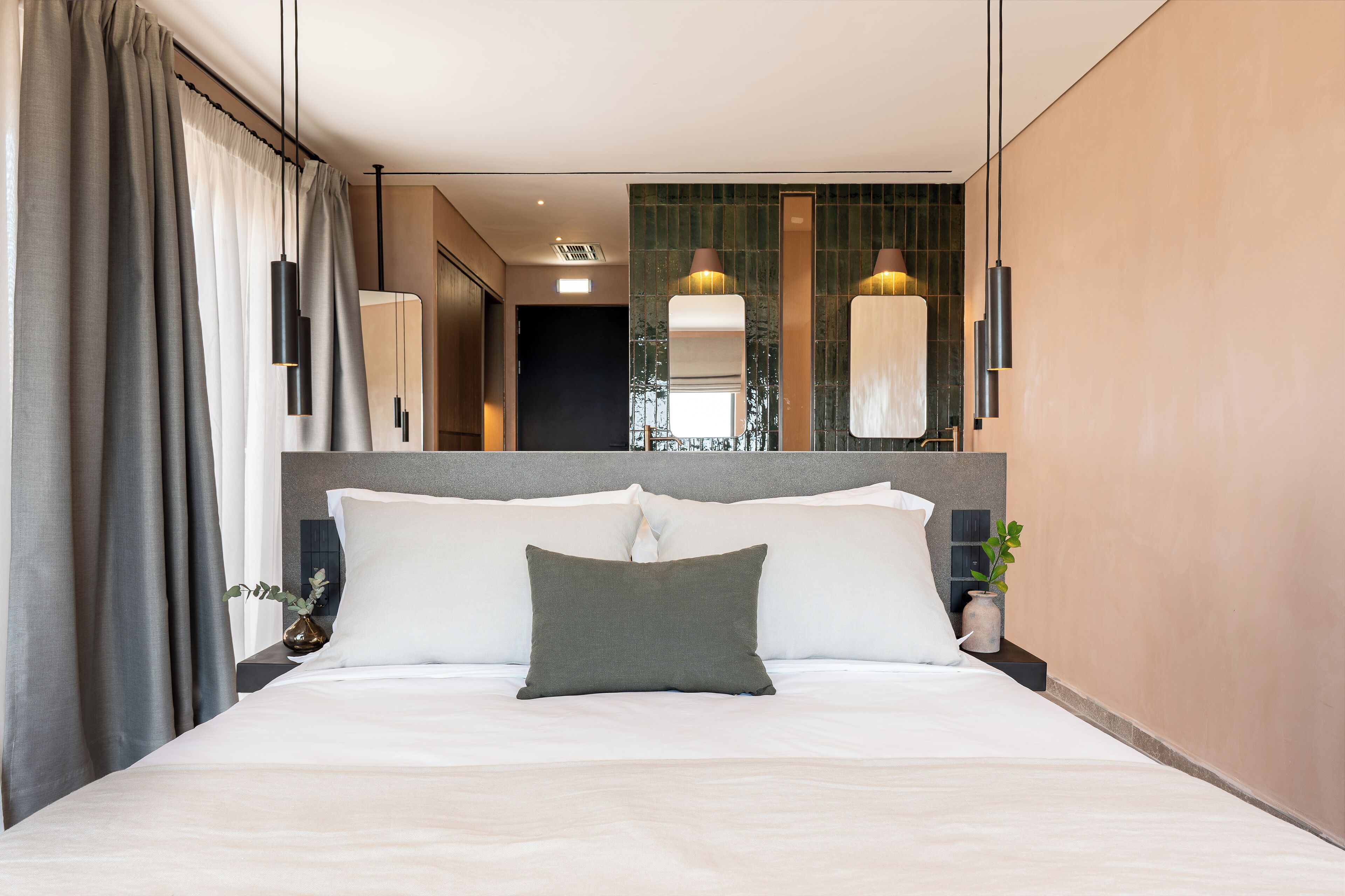 A modern hotel room with a large bed, a headboard, and a nightstand with a vase.